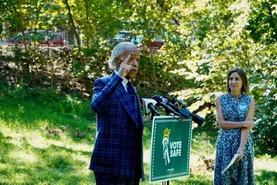 Rev. Al Sharpton points as he speaks beside the Vote Safe sign with Randi Weingarten looking on