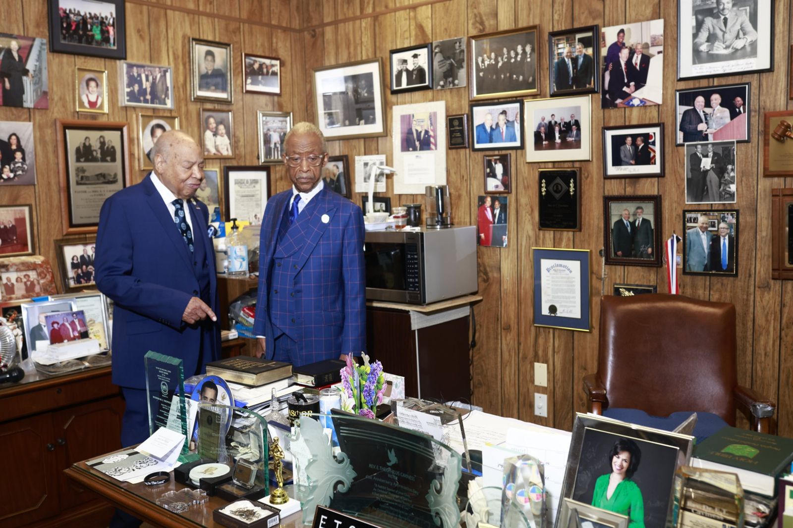 Bishop Caviness shares memories with Rev. Al Sharpton beside a desk of awards and photographs