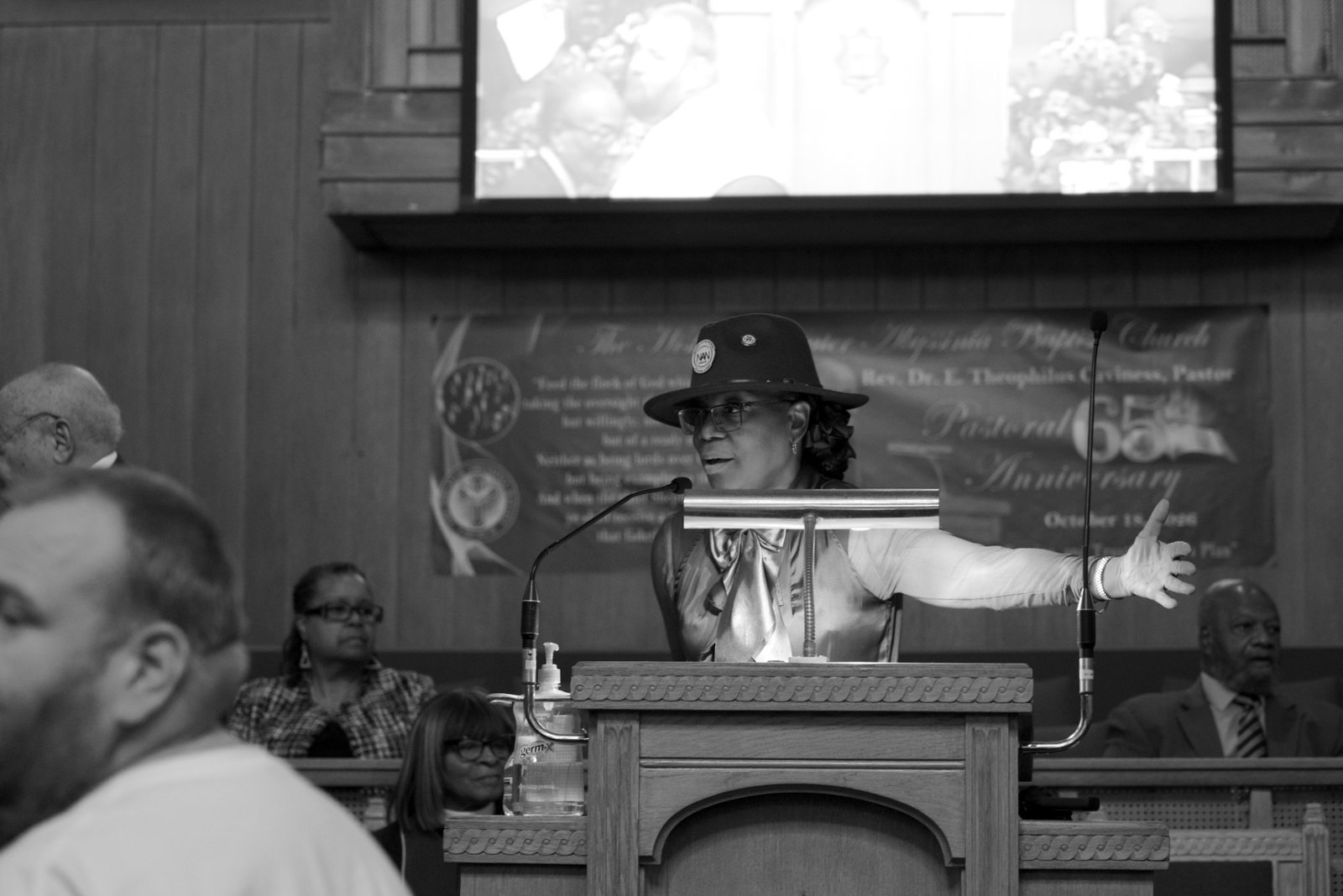A NAN leader speaks from the podium, in black and white, beneath the 65th Anniversary banner