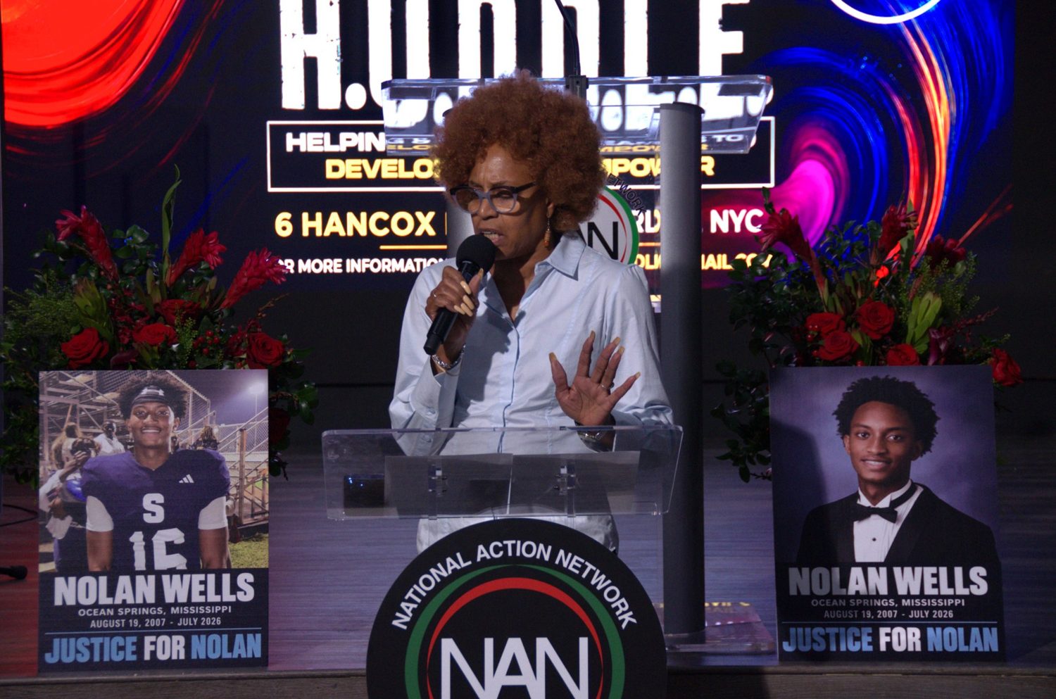 A speaker stands between the Justice for Nolan posters at the Youth Huddle